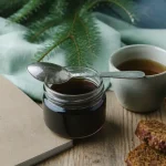 Miel de sapin bienfaits : pot sombre et cuillère, gorge et vitalité